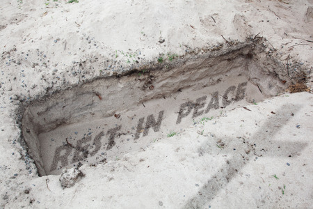 Open grave in the desert. In  the desert sand are written the words rest in peace. Concept for human deathの写真素材