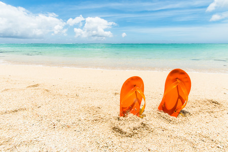 travel background with a pair of orange flip-flops in the sand of a beautiful beach, Mauritius, Africaの写真素材