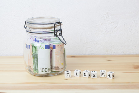preserving glass with Euro banknotes and letter cubes with the german word Zinsen on a wooden board, financial concept for saving money and interestの写真素材