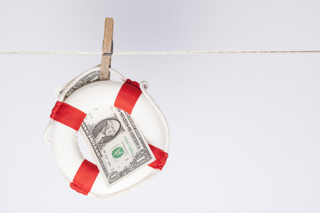 clothespin fixing a safety buoy with a one dollar banknote on a clothes line. financial concept for currency risk or protectionの写真素材