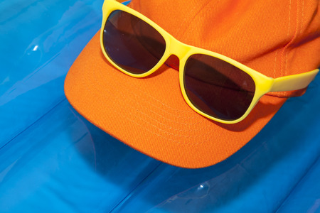 orange base cap with yellow sunglasses on a blue air mattress, concept for summer vacation ans holidayの写真素材