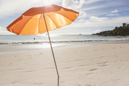 orange sunshade in bright sunlight at a tropical beach, travel concept for summer, vacation and sun protectionの写真素材