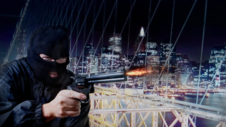 skyline of a city at night and a black masked criminal shooting with a revolver; social concept for urban crime and violenceの写真素材