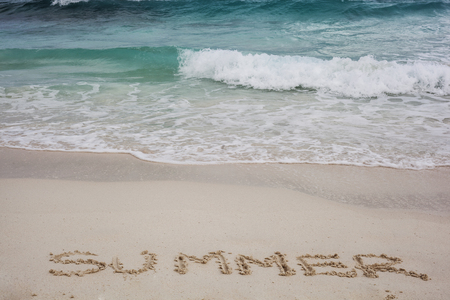 travel background with the waves of the sea,  a beach and the word summer written in the sandの写真素材