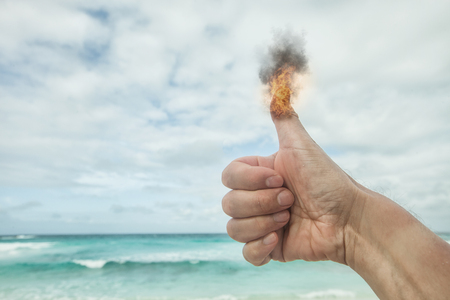 burning raised thumb of at the ocean under a cloudy sky, concept concerning tourism or social mediaの写真素材
