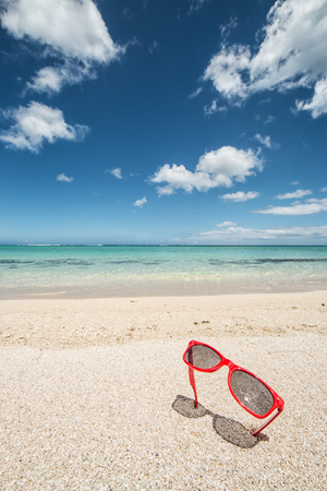 vertical travel background with red sunglasses in the white sand of a tropical beach a turquoise sea and blue sky, concept for travel and vacationの写真素材