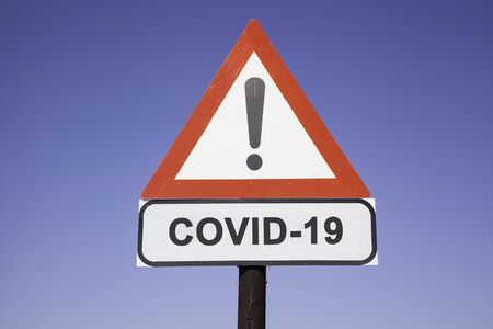 White road warning triangle with black  exclamation point and red frame on  a wooden mast in front of a blue sky. A second rectangular sign warns about  SARS-COV-2 virus epidemic or pandemicの写真素材