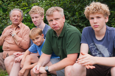 Grandfather sitting on a bench with his son and grandchildrenの写真素材