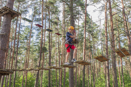 A boy wearing a safety harness and a helmet walking in a rope park.のeditorial素材