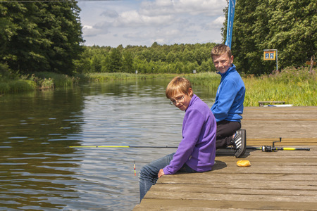 Spychowo, Poland - July 23, 2015: Young boys sitting on a wooden bridge and fishing.のeditorial素材