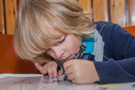 Jozefow, Poland - October 24, 2015: A boy with long blond hair is writing something with markers pensのeditorial素材