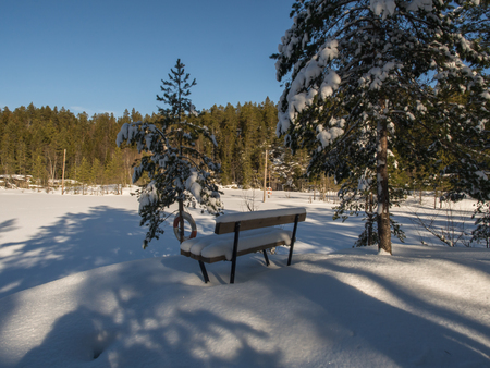 A snow covered bench at the shore of a frozen lakeの写真素材