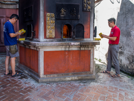 Tainan, Taiwan - October 11, 2016: Men throwing ghost money into a stove in a Taoist templeのeditorial素材