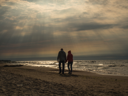 Young couple walking along a shore of the sea at sunset timeの写真素材