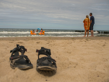 Mielno, Poland - July 31, 2016: Parents / pair standing on a shore and watching their children bathing Mielno, Poland - July 31, 2016: Parents / pair standing on a shore and watching their children bathing