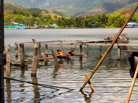 Sentani,  Indonesia - January 24, 2015: Children play happily jumping from a bridge into the water on the shore of Sentani Lakeのeditorial素材