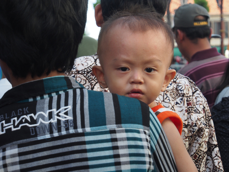 Jakarta, Indonesia - January 11, 2015: Small Indonesian child, with beautiful eyes, carried through the crowded streets by the parent.のeditorial素材