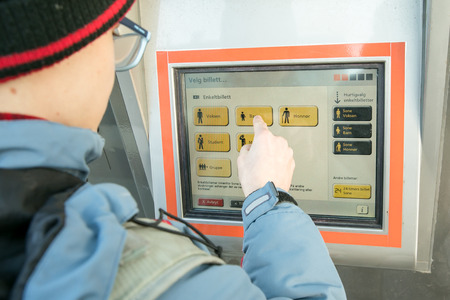 The boy buys a ticket at the color ticket booth and information point at the tram stop in Bergen,...