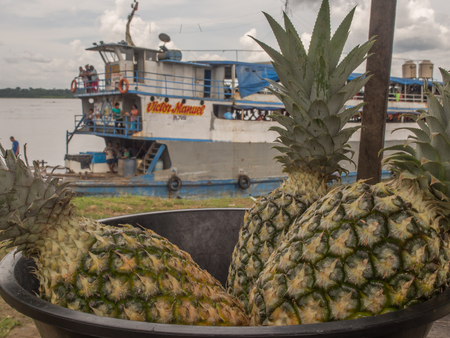 Amazon River, Peru - December 11, 2017: Pineapple in a bowl on the background of a cargo boat on the Amazon riverのeditorial素材