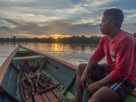 Jungle, Brazil - Dec 7, 2017:  Portrait of a man with a red skin sitting on the boat on the backgroud of sun set.  Amazon  jungleのeditorial素材