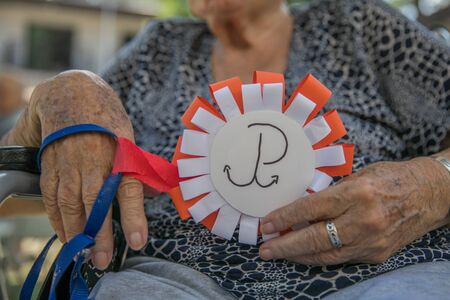 Hands of old woman with  white and red cotillion with superposed anchor emblem of the Polish...