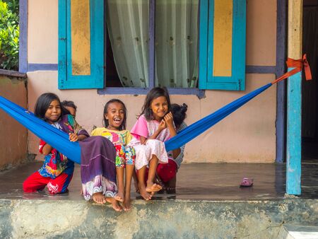 Ambon, Indonesia - February 11, 2018: A group of young Indonesian girls, in colorful clothes sitting on the hamak in the small village on the island, Maluku, Malukiのeditorial素材