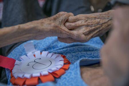 Hands of old woman with  white and red cotillion with superposed anchor emblem of the Polish resistance. Anniversary of the Warsaw Uprising. Polish symbols.のeditorial素材