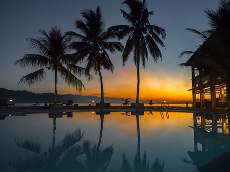 View with silhouettes of  palm trees around luxury swimming pool during a tropical sunset. Ambon Island. Indonesiaの写真素材