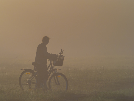Silhouette of the woman with bicycle  during the foggy morning. Bug River.  Podlasie. Podlachia. Poland, Europe. The region is called Podlasko or Podlasze. Panoramic view.の写真素材