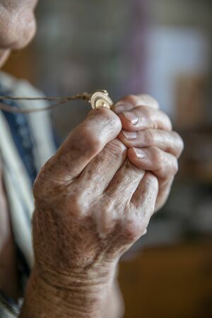 Hands of an old woman praying and holding a gold medal with Our Ladyの写真素材