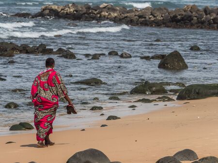 A figure of a Muslim woman in a red boubou walkingby the ocean shore. Senegal. Africa.の写真素材