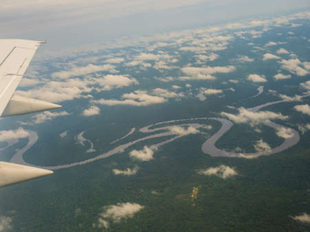 View from airplane window. Wing of an airplane flying above the clouds over Amazon River. Top View...