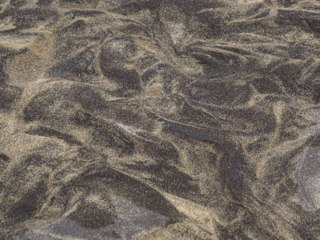 Background, texture. Patterns on yellow-black sand covered with water of a flowing brook. Lofoten....