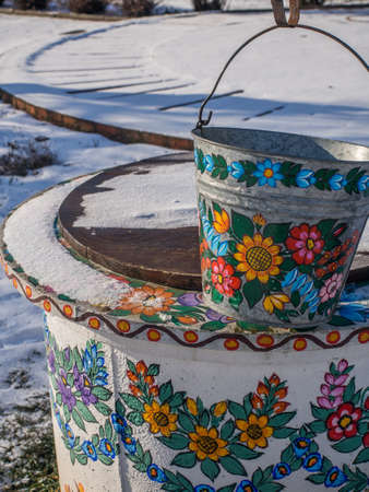 Zalipie, Poland - May 20, 2017: A manually painted metal bucket over a well in the colorful village - Zalipie, heritage park where all buildings and objects are decorated with traditional floral motif. Winter time. Eastern Europe.のeditorial素材