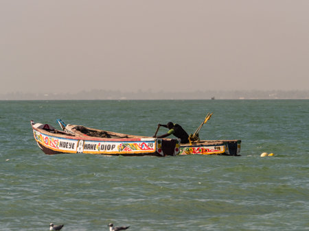 Nianing, Senegal - January 24, 2019: Colorful wooden fishing boats bouncing on the waves anchored far from the beach. africaのeditorial素材