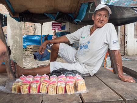 Iquitos, Peru - December 2019: Portrait of an old man sitting on the table and selling cakes at the Belen bazaar (BelÃ©n market), Iquitos - gate to the rainforest, Amazonia, Loreto, South Americaのeditorial素材