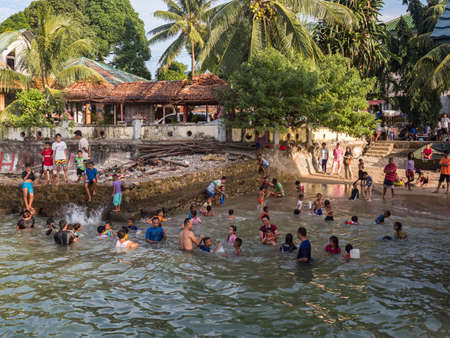 Ambon, Indonesia - February 2018: Many children play and swim in the bathing area at the city beach in the coastal town of Ambon. Ambon Island, Maluku Archipelago, (Moluccas) Indonesia. Asiaのeditorial素材