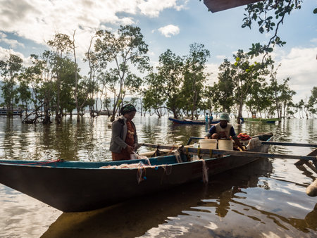 Kaimana, West Papua, Bird's Head Peninsula, Indonesia - February, 2018: A local family is removing fish from the net while standing in the water next to a small wooden boat. Lifestylesのeditorial素材