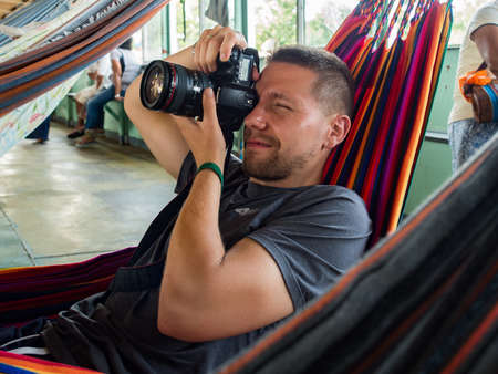 Amazon River, Peru - Sep, 2019: Young caucasian man with camera and many beautiful, colorful hammocks on the cargo boat. Amazonia, trail from Santa Rosa to Iquitos. Amazon River, Peru. South Americaのeditorial素材