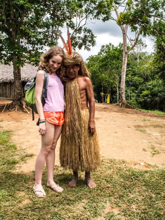 Iquitos, Peru- May 2016: Yagua Senior Indian in his local costumee with young white girl. Amazon....
