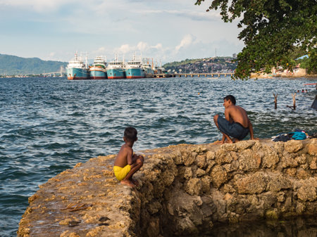 Ambon, Indonesia - February 2018: Many children play and swim in the bathing area at the city beach in the coastal town of Ambon. Ambon Island, Maluku Archipelago, (Moluccas) Indonesia. Asiaのeditorial素材
