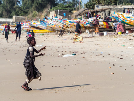 Senegal, Africa - January, 2019: Portrait of a small black girl on the beach. Wooden boats in background. Senegal, Africa.のeditorial素材