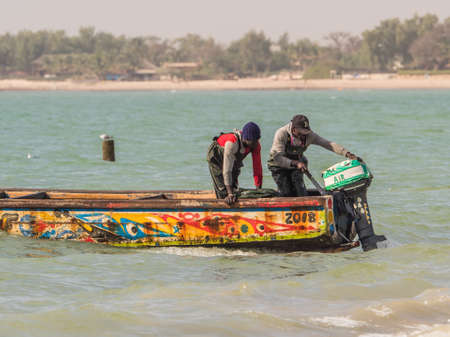Nianing, Senegal - January 24, 2019: Colorful wooden fishing boats with fishers bouncing on the waves anchored far from the beach. Africaのeditorial素材