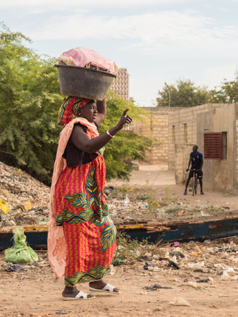 Senegal, Africa - Jan, 2019: Senegalese woman with a bucket on her head on the street.のeditorial素材