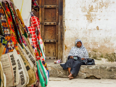 Stone Town, Zanzibar, Tanzania - January 2021: Pensive elderly African woman sitting between the stone walls of Africa cityのeditorial素材