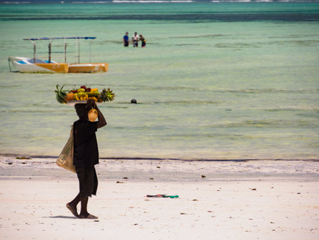 Paje, Zanzibar, Tanzania - January 202: African with a tray full of exotic fruits on his head. Turquoise ocean water in the background. Africaのeditorial素材