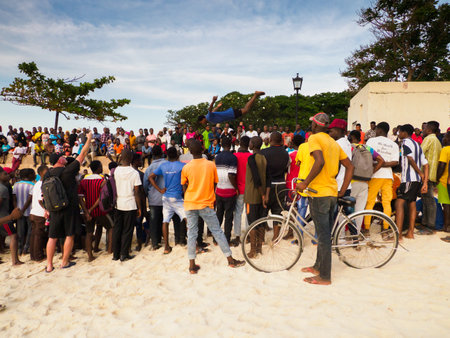 Stone Town, Zanzibar, Tanzania - January 2021: Crowds of people watch like young people jump on an inner tube on a sandy beach in Stone Town. Africaのeditorial素材
