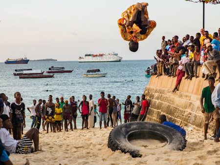 Stone Town, Zanzibar, Tanzania - January 2021: Crowds of people watch like young people jump on an inner tube on a sandy beach in Stone Town. Africaのeditorial素材