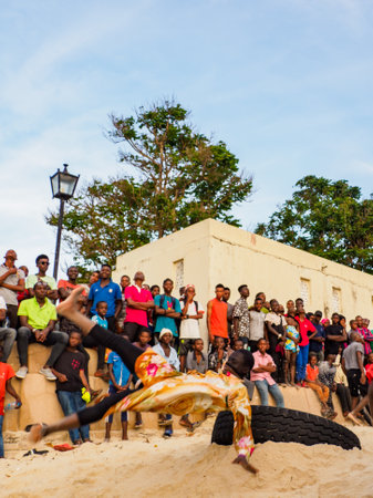 Stone Town, Zanzibar, Tanzania - January 2021: Crowds of people watch like young people jump on an inner tube on a sandy beach in Stone Town. Africaのeditorial素材