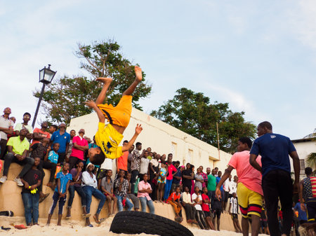 Stone Town, Zanzibar, Tanzania - January 2021: Crowds of people watch like young people jump on an inner tube on a sandy beach in Stone Town. Covid-time.. Africaのeditorial素材